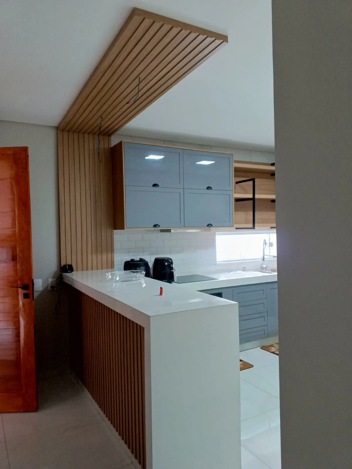 Cozinha cinza com bancada branca e forro ripado em madeira